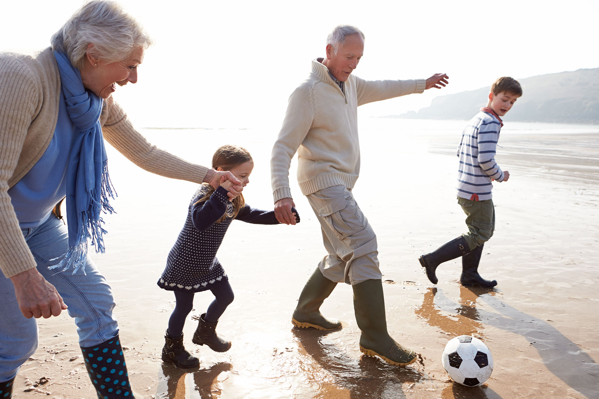 Two elderly people and two children playing ball on a beach