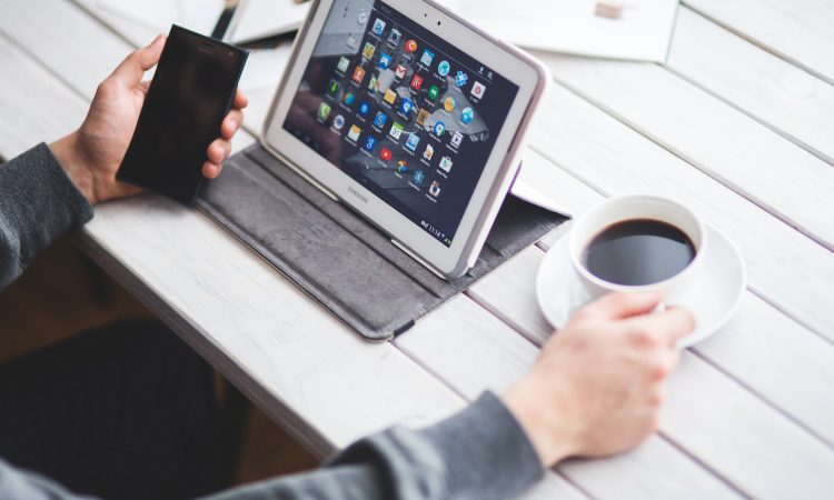 Personne prenant son café devant sa tablette et son cellulaire