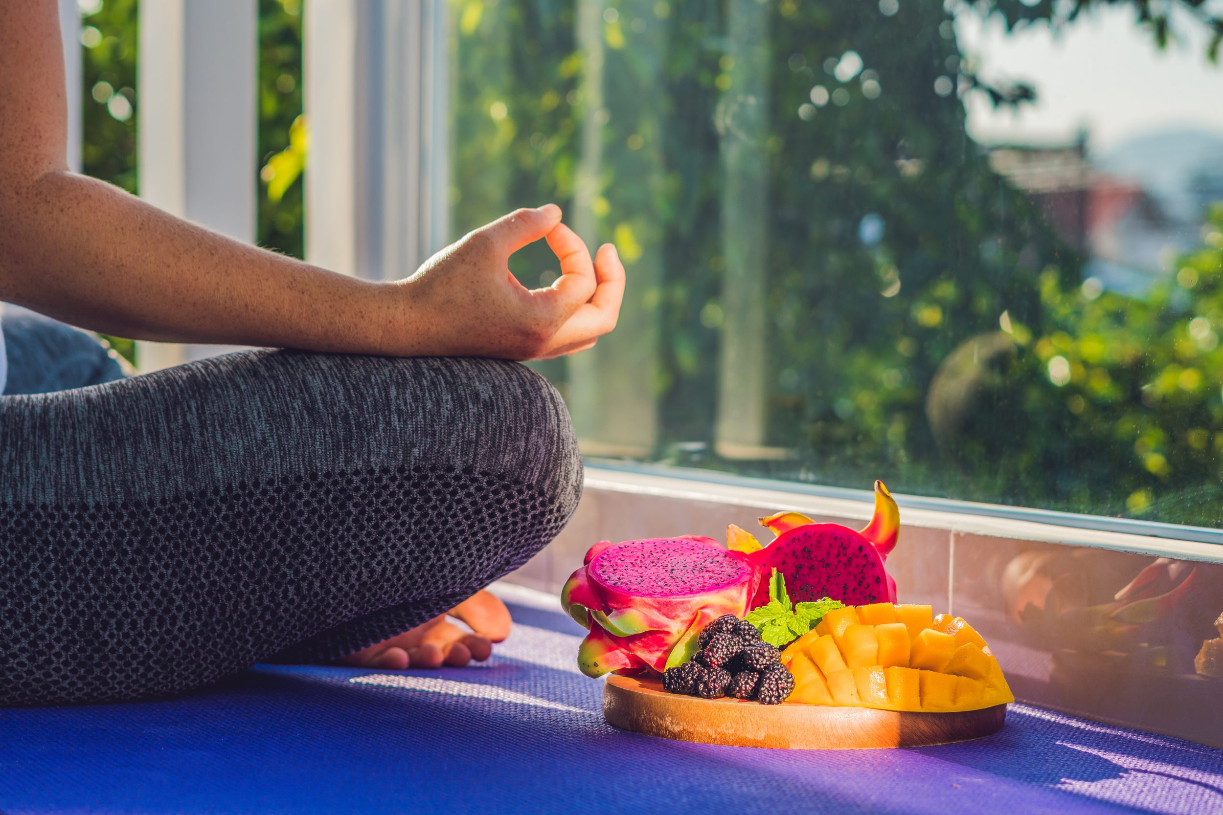 femme en position de yoga avec une assiette de fruits