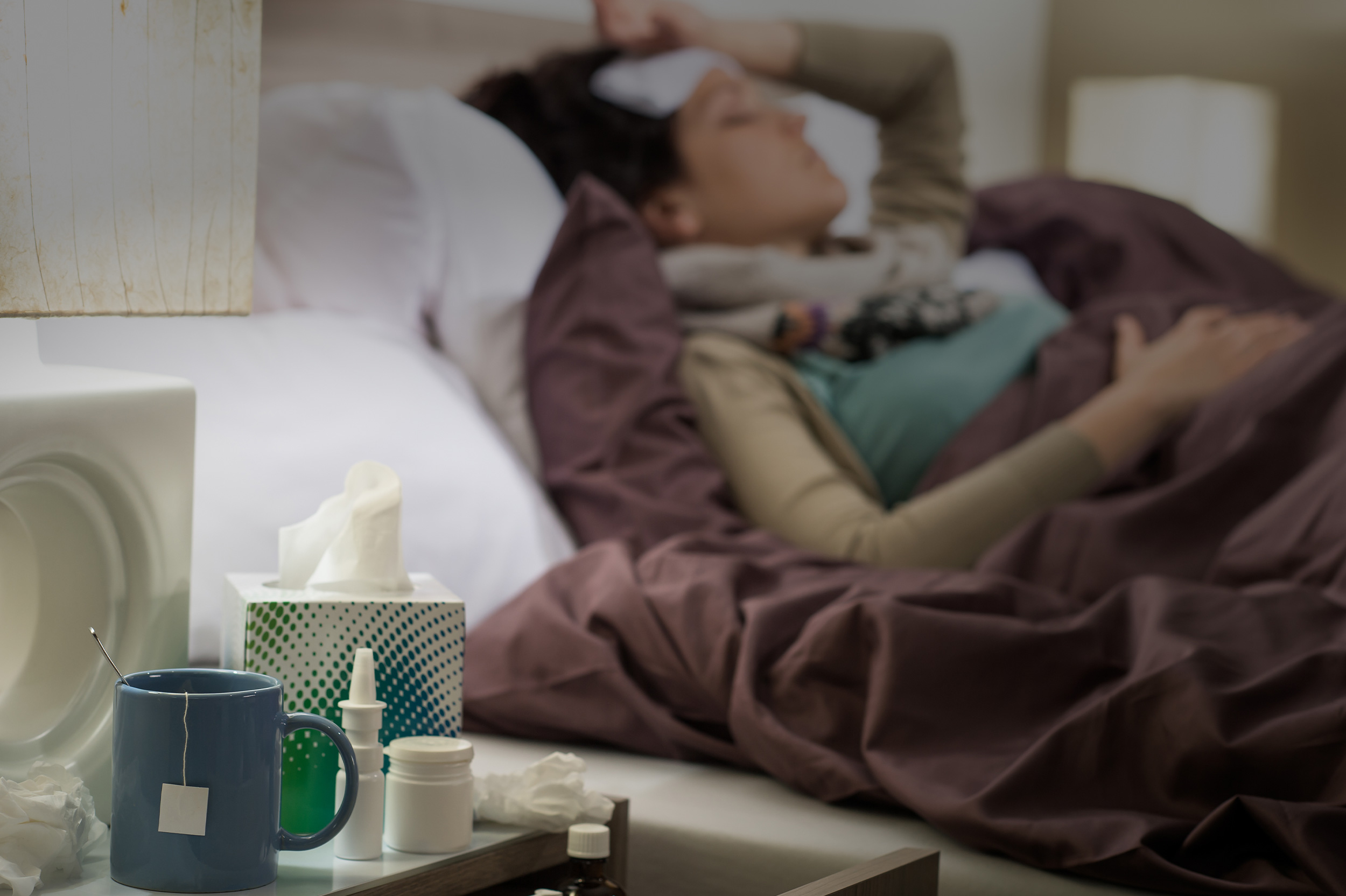 femme couchée dans son lit avec des médicaments contre le rhume et la grippe